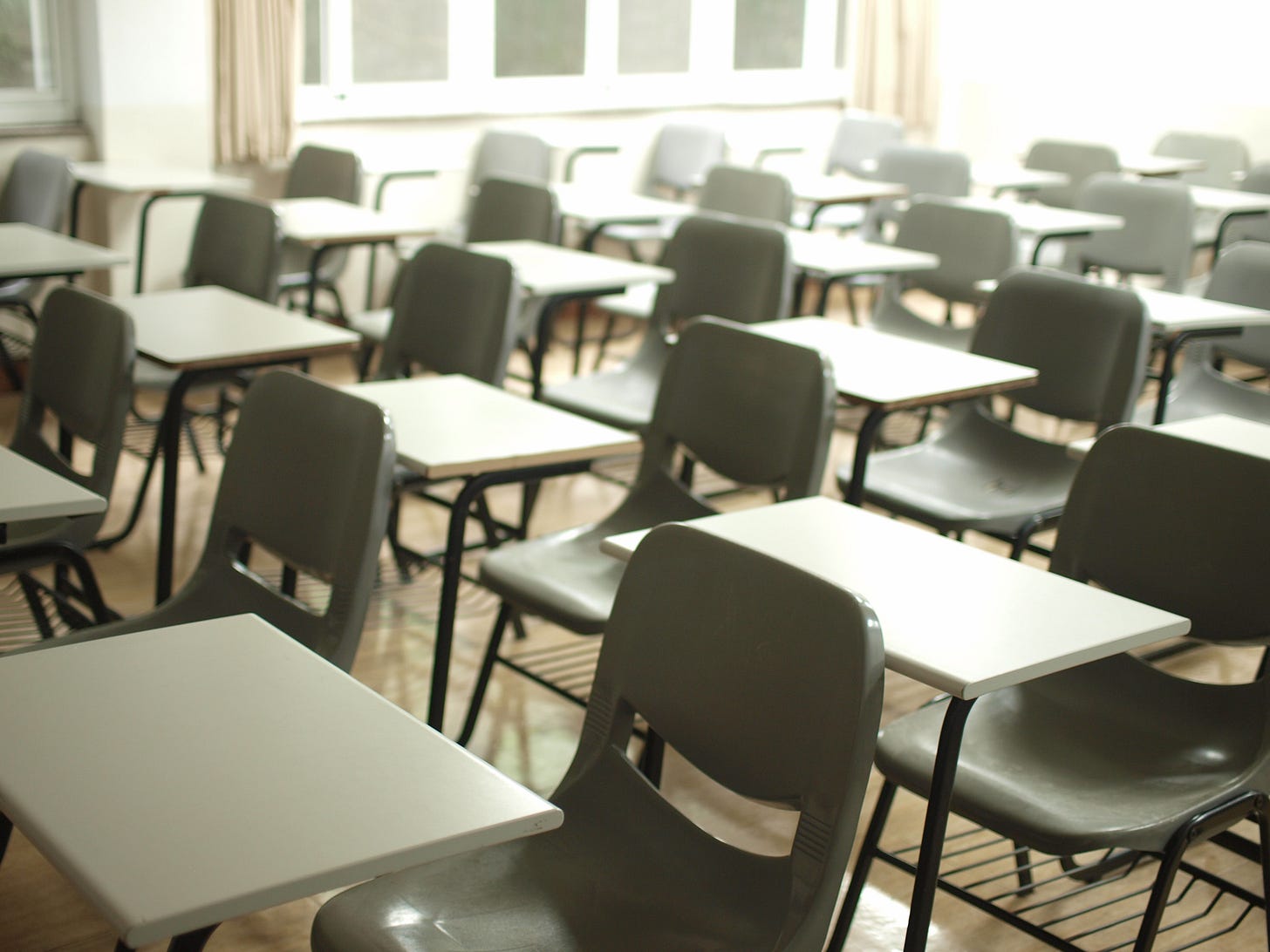 Rows of single desks with chairs in a sunlight filled classroom