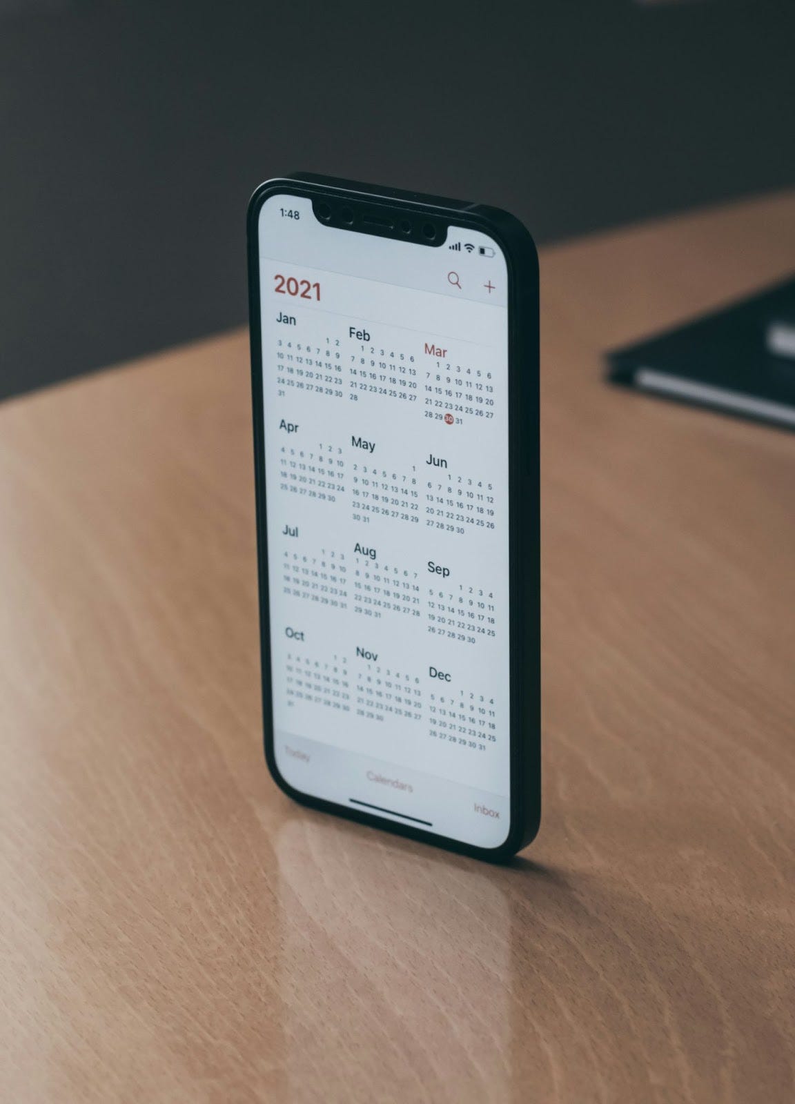 A phone balanced standing on a desk, showing the year 2021 month by month, day by day. A phone balanced standing on a desk, showing the year 2021 month by month, day by day.