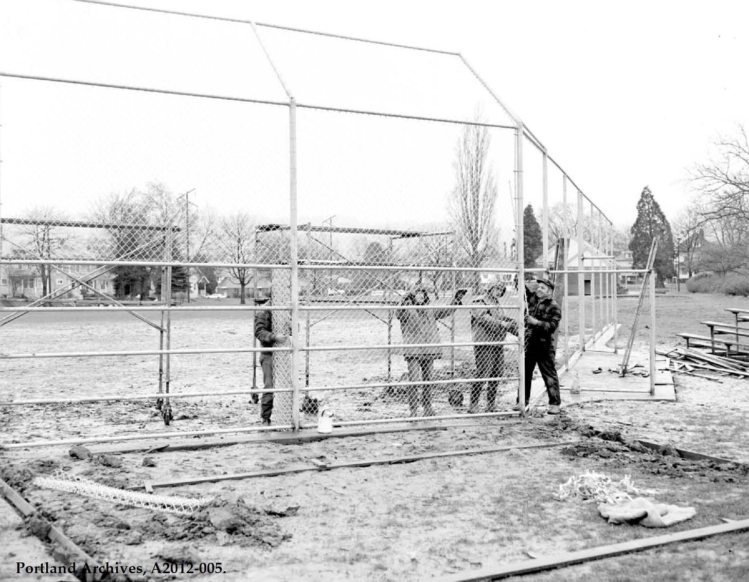 Black and white photo of people installing baseball backstop