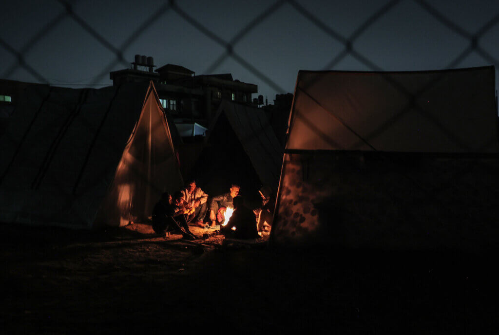 Palestinian refugees huddle around a fire in a camp in Rafah in the southern Gaza Strip. Over a million Gazans have been displaced since Israel began its bombardment of the Strip in October 2023.