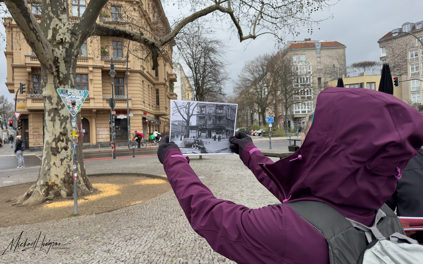 The author looks at a newsreel photo showing the same tree she is standing in front on a Berlin Battle Damage tour.