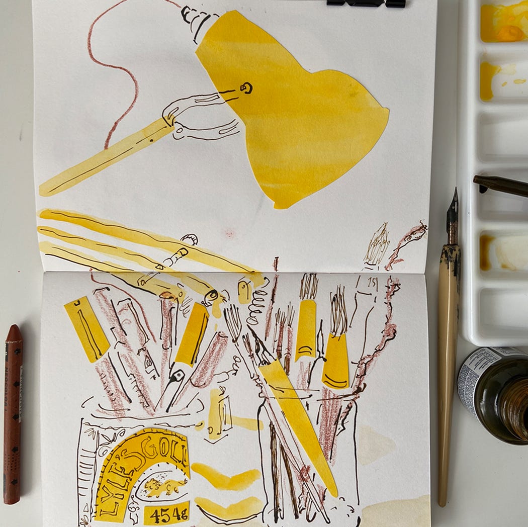 An open sketchbook surrounded by art materials. On the sketchbook pages is a painting in loose yellow shapes of a desk lamp and pens and brushes in jars, with outlines of pen and ink drawing.