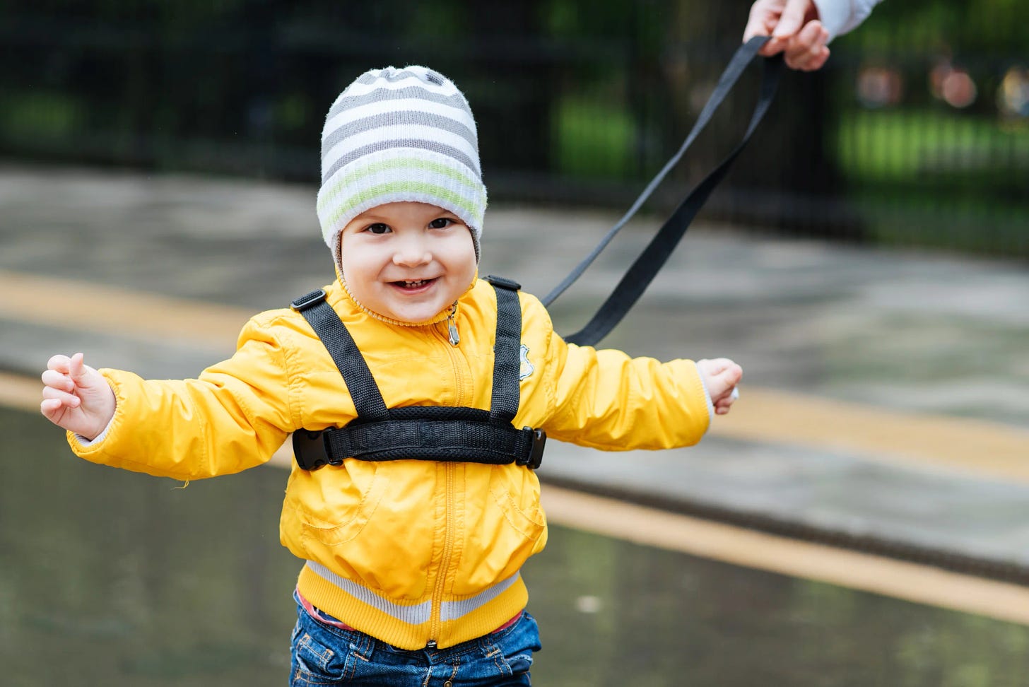 Picture of a young white child wearing a yellow jacket, multicolored hat and a safety harness