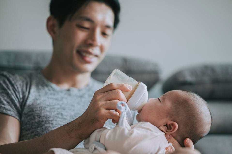 Asian Chinese young father feeding his baby boy son with milk bottle at living room during weekend