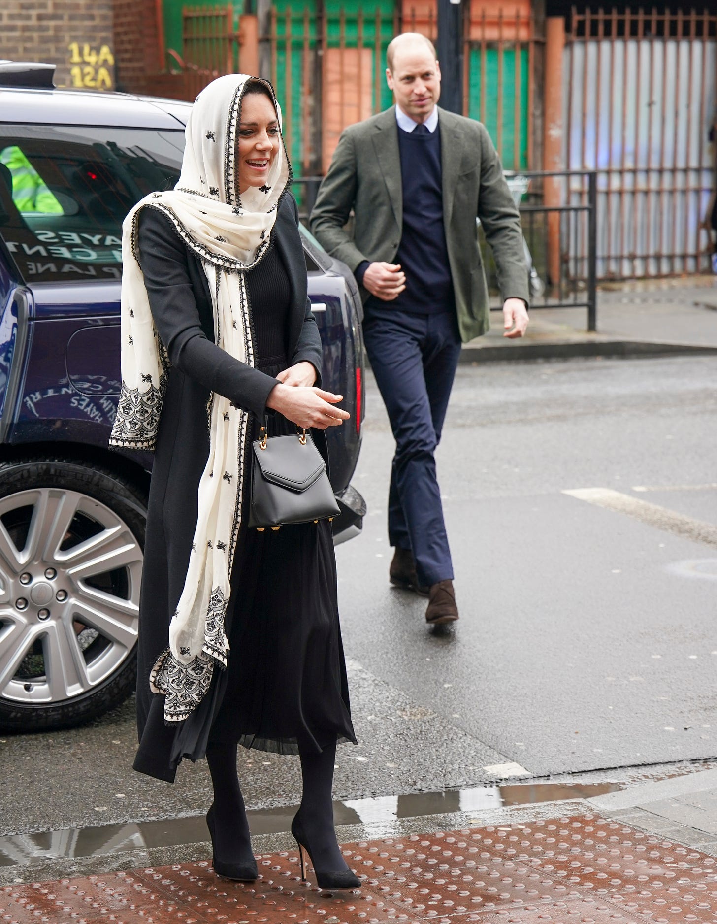 Princess of Wales wearing a headscarf with Prince William in the background