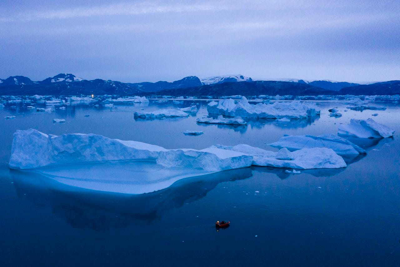A small boat is shown in the water with lots of icebergs of varying size.