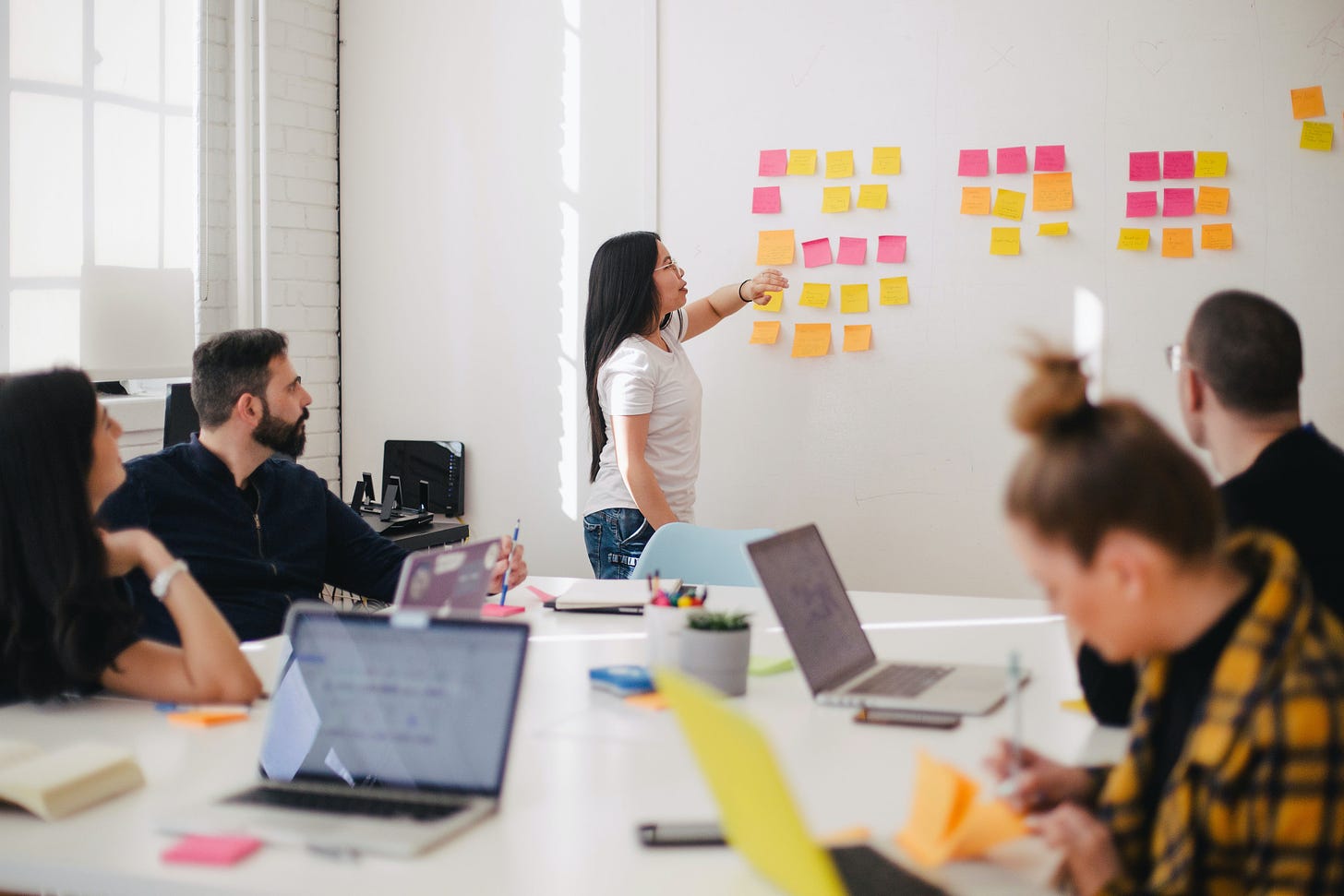 Person presenting to other colleagues with a wall full of post-it notes behind her