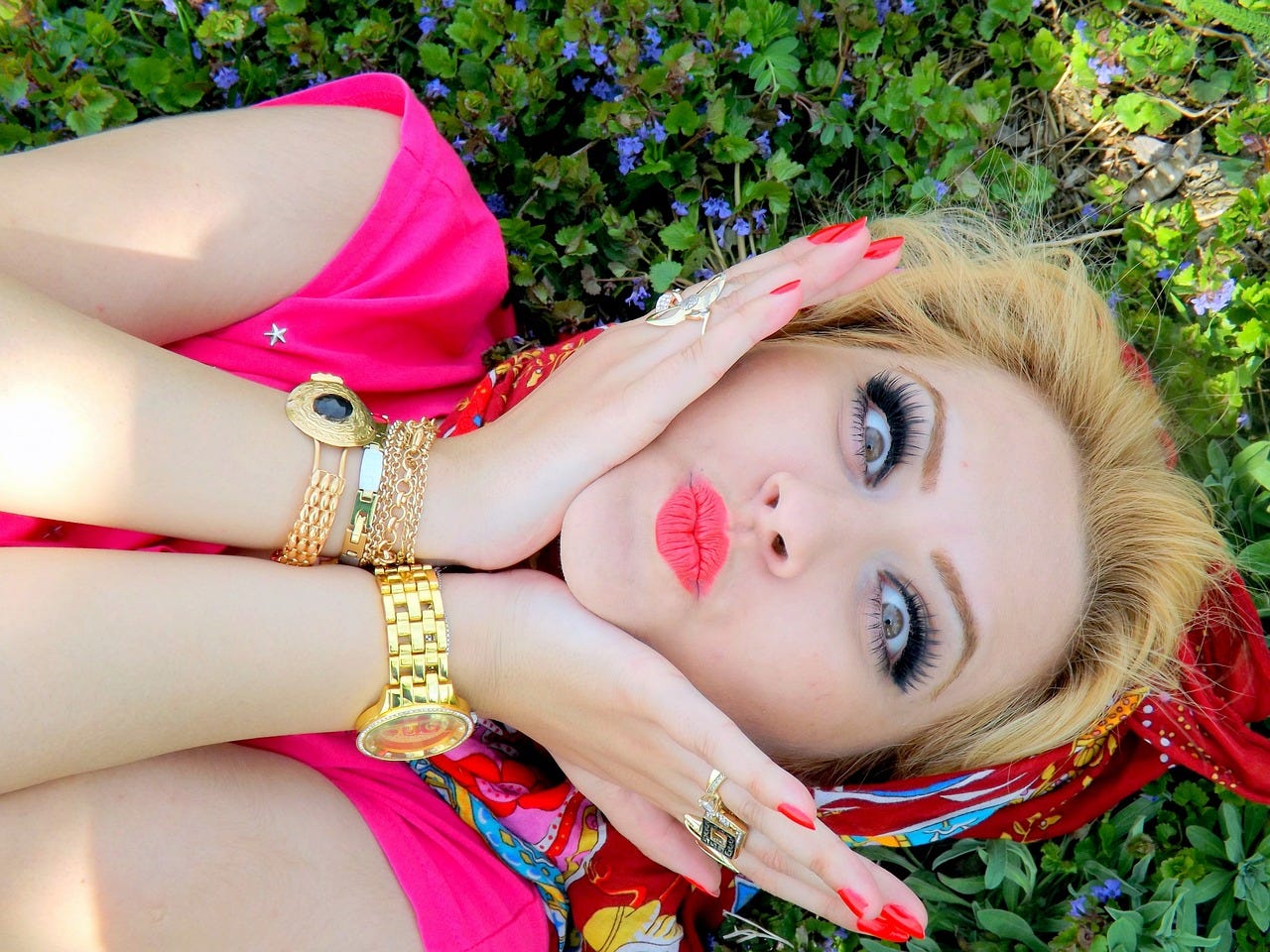 A woman lying on the ground looking up at the camera with pursed pink lips and wide eyes.