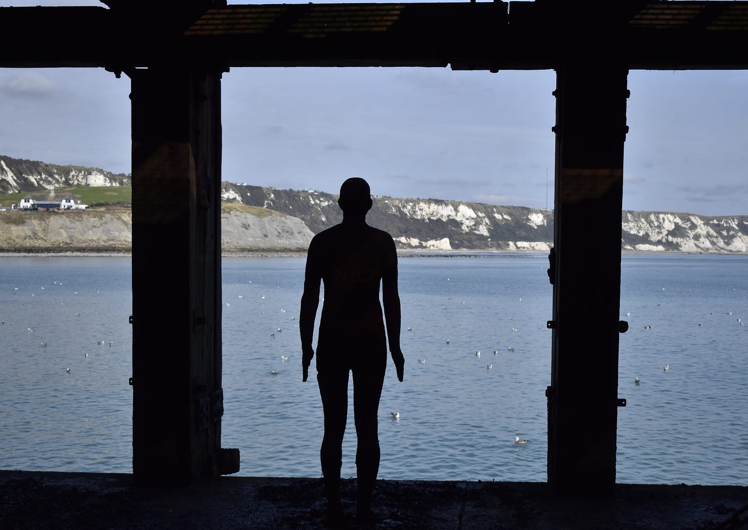 Anthony Gormley Statue under the pier at Folkstone. Looking out over the water and chalk cliffs