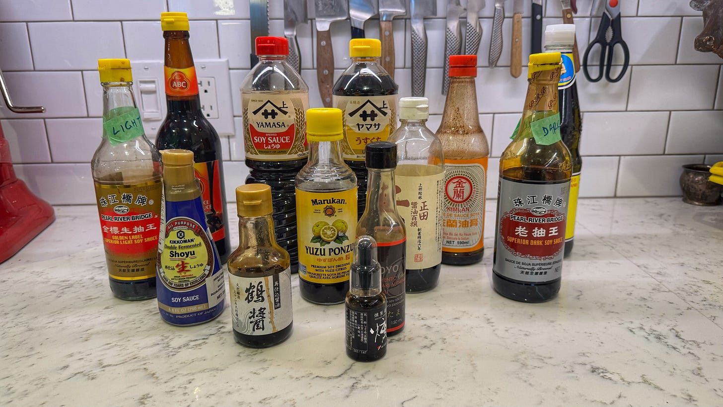 All thirteen of the soy sauces I own, randomly arranged on a kitchen counter