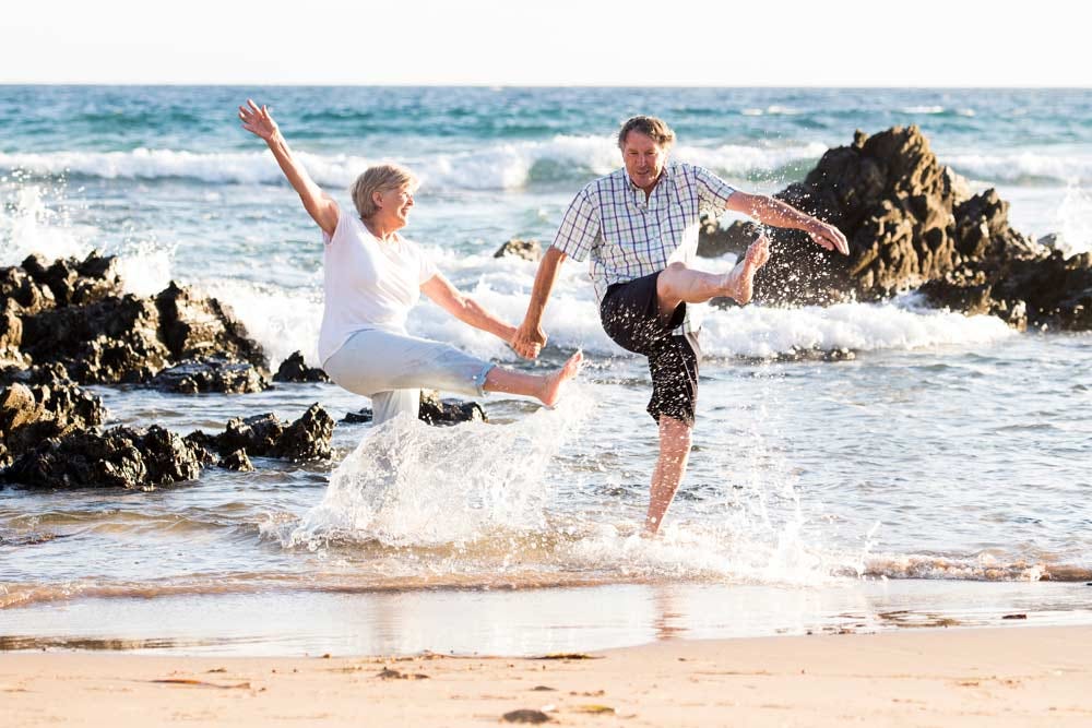 Senior couple walking happy & relaxed on the beach together.