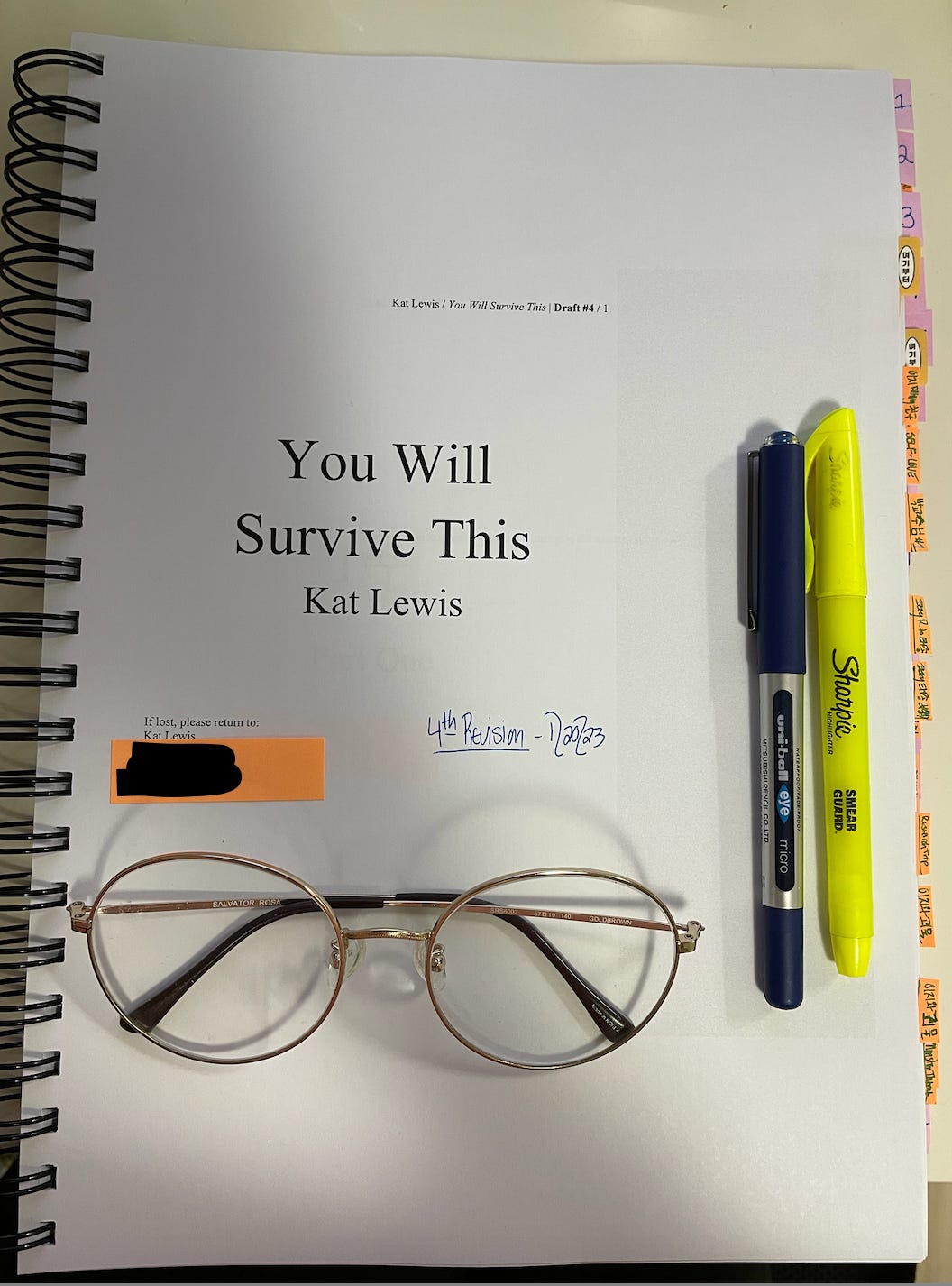 A photo of Kat’s printed manuscript for You Will Survive This. The manuscript is turned to the titled page. Tabs of various colors along the side of the print out indicate chapter numbers and revision notes. The notes are written in both English and Korean.