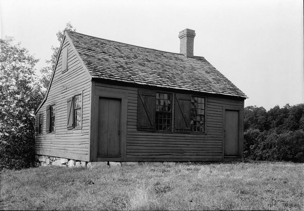 Wooden building with doors on each end of one side, glass window panes, wooden shutters, and one chimney and a field stone foundation.