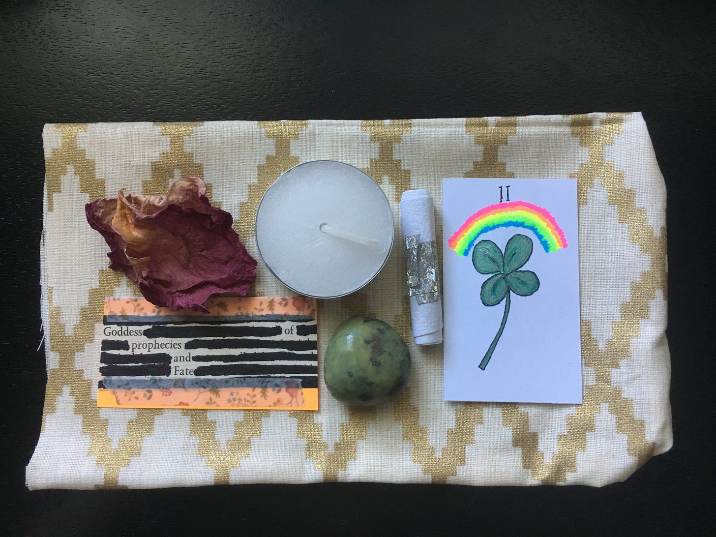 A spell kit with a rose petal, candle, Lenormand card with four-leaf clover, crystal, and blackout poem