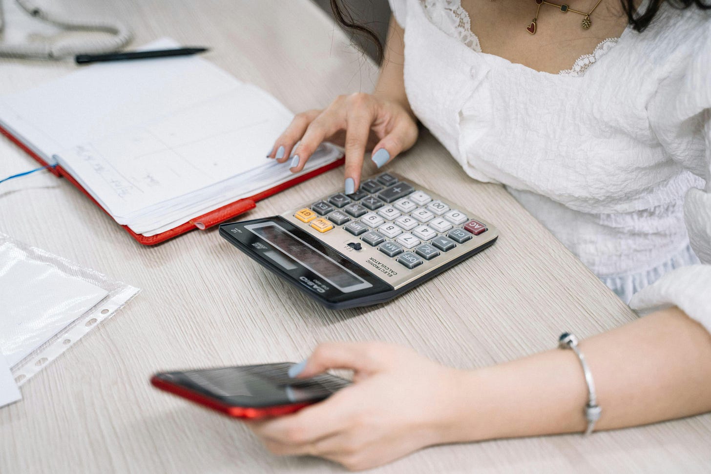 Woman using a calculator, with a notebook on her desk. Woman using a calculator, with a notebook on her desk.