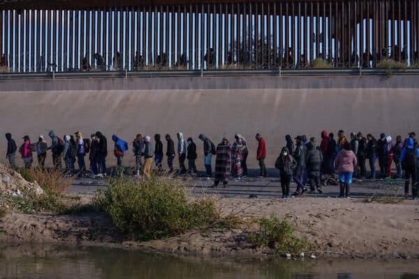 A group of migrants near a border fence.