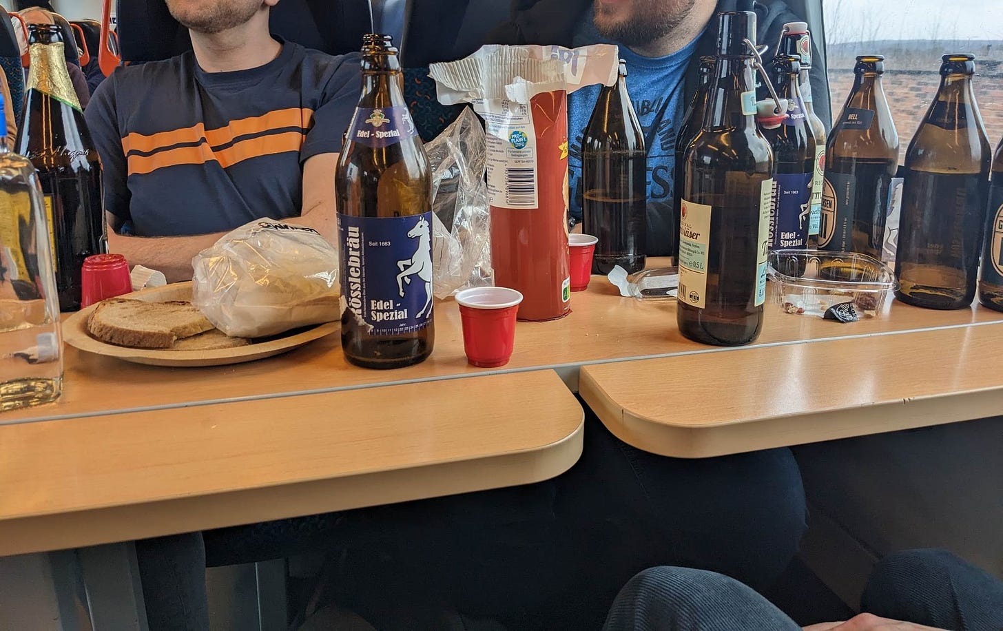 two men (faces cut off) at a train table covered in beer bottles and snacks