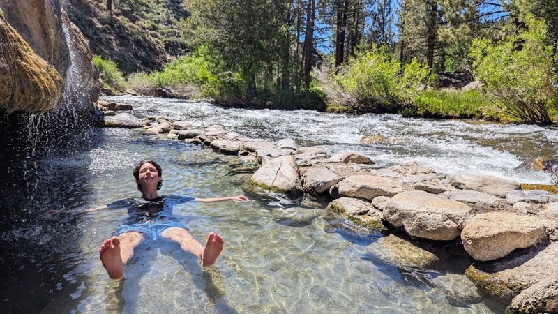 Rey, a white nonbinary person wearing a t-shirt and swim trunks, floating, head back and eyes closed in the warm water