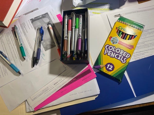 A cluttered desk, with many pens and pencils in lots of colors.