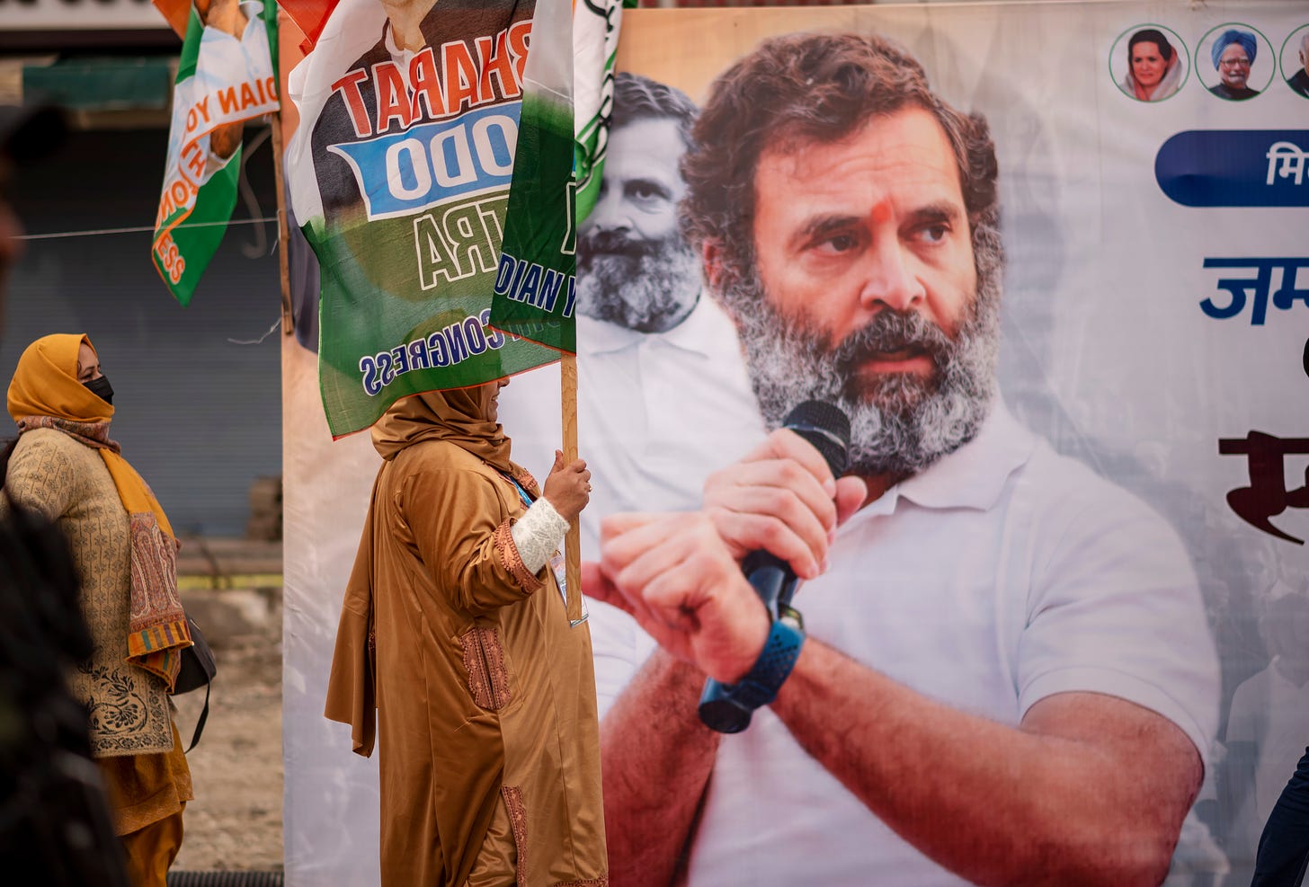 Srinagar, Jammu and Kashmir: A supporter of India’s Congress party holds a flag while walking past a billboard depicting Congress leader Rahul Gandhi during his 4,000 km march across the country. (Photo by Idrees Abbas/SOPA Images/LightRocket via Getty Images)