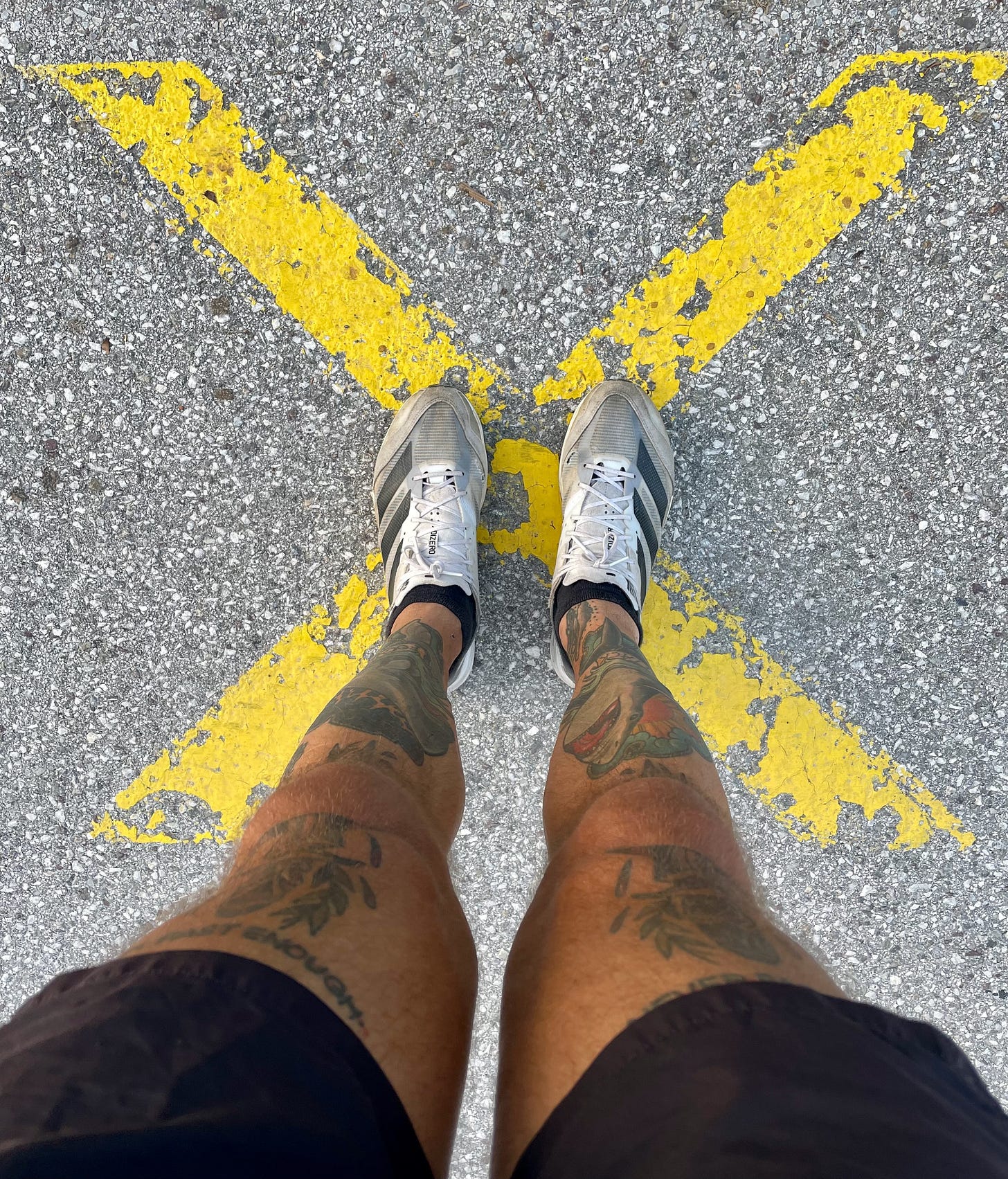 the author's legs standing on a yellow x on an asphalt road