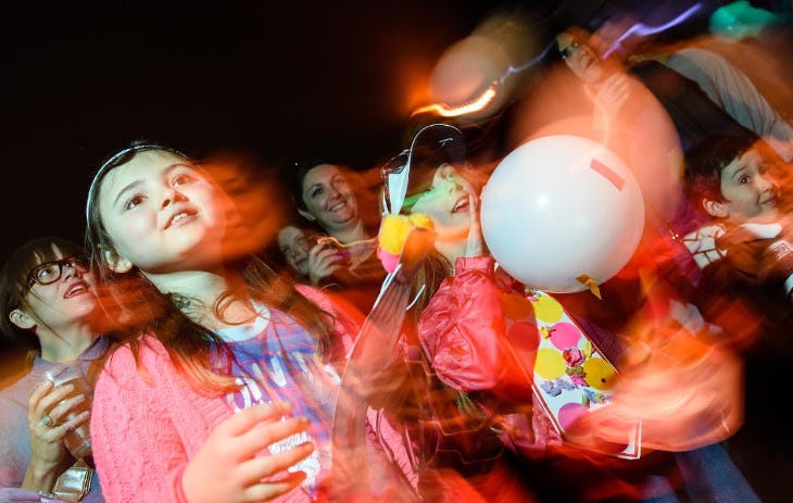 Adults and children on a dancefloor, with balloons