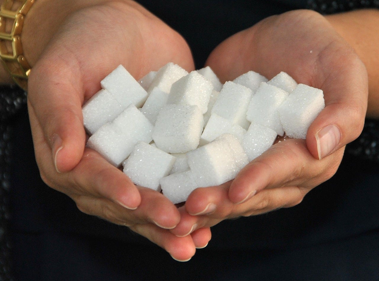 Two cupped white hands full of white sugar cubes, on a black background