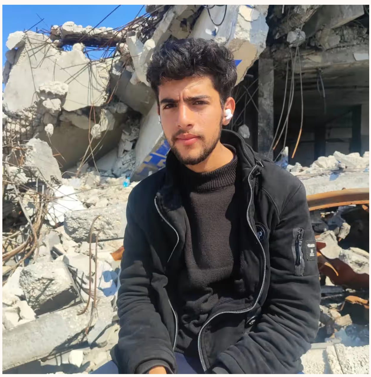 image of Sha'ban al-Dalou via his Instagram. A young light brown skinned Palestinian man in a black hoodie and brown sweater sits in front of a pile of rubble. Photograph: Instagram via @shabanahmed19