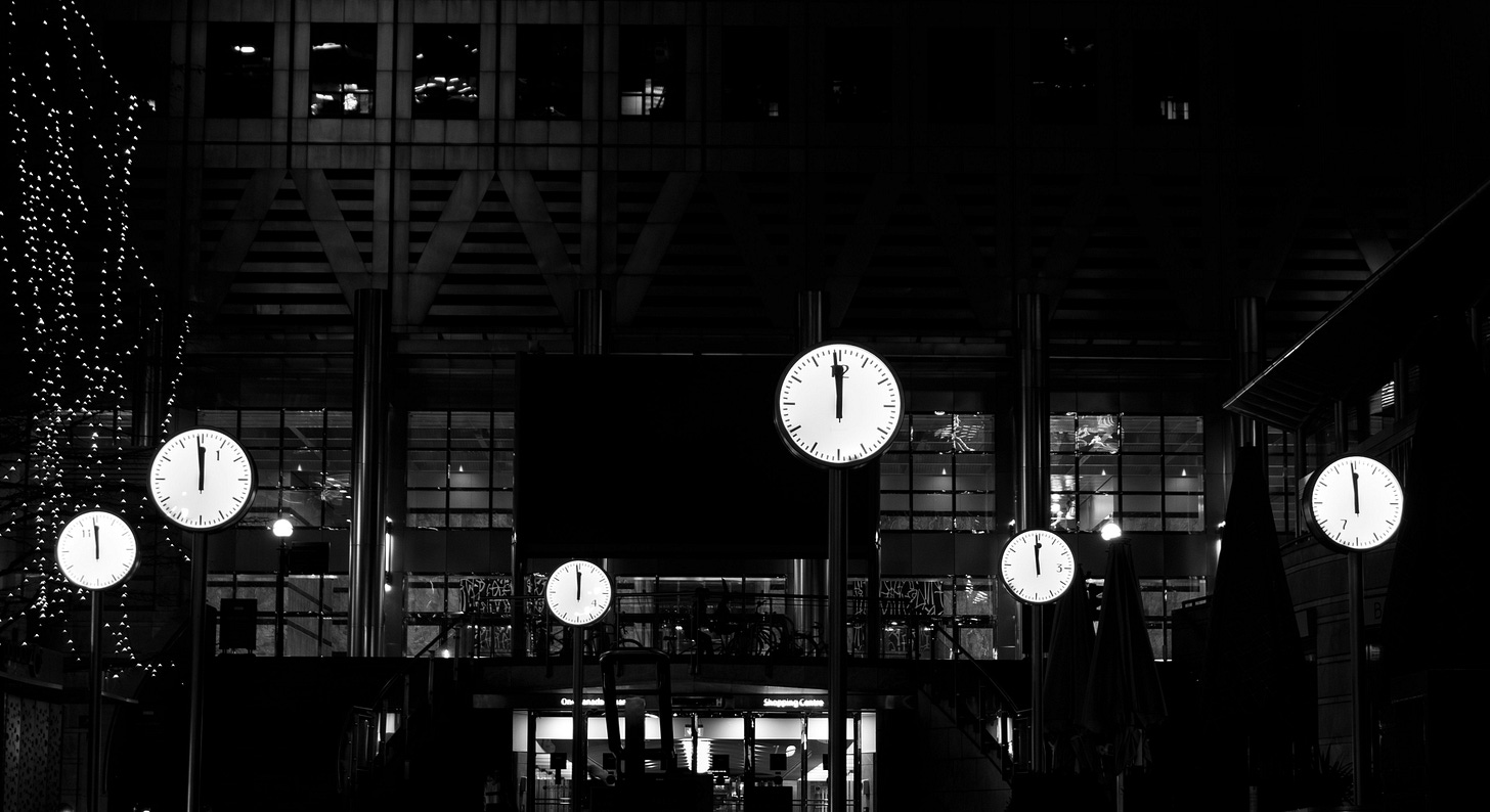 A black and white photo of a plaza with six white clock faces reading midnight