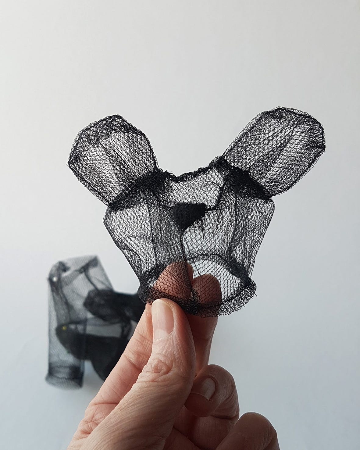 a hand holding a small mock-up of a teddy bear made of transparent black tulle