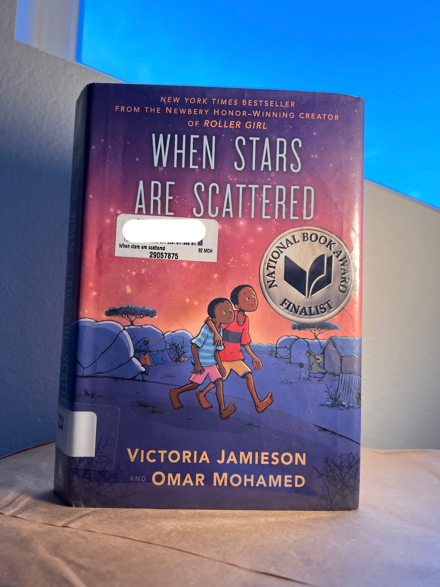 When Stars Are Scattered, National Book Award finalist. Two boys with brown skin and black hair walk with their arms around each other under a pink, star-lit sky.