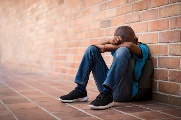 Young sad boy at school Young boy sitting alone with sad feeling at school. Depressed african child abandoned in a corridor and leaning against brick wall. Bullying, discrimination and racism concept at school with copy space. young black boy sad stock pictures, royalty-free photos & images