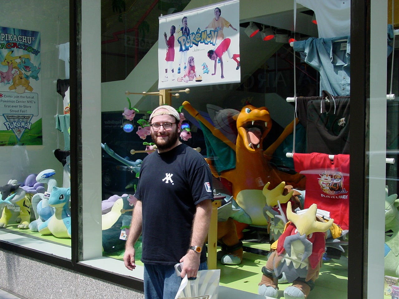 Tatton’s friend outside of the Pokémon Center New York store on July 22nd, 2002. The window display has various plush toys, clothing, and a huge six-foot Charizard statue