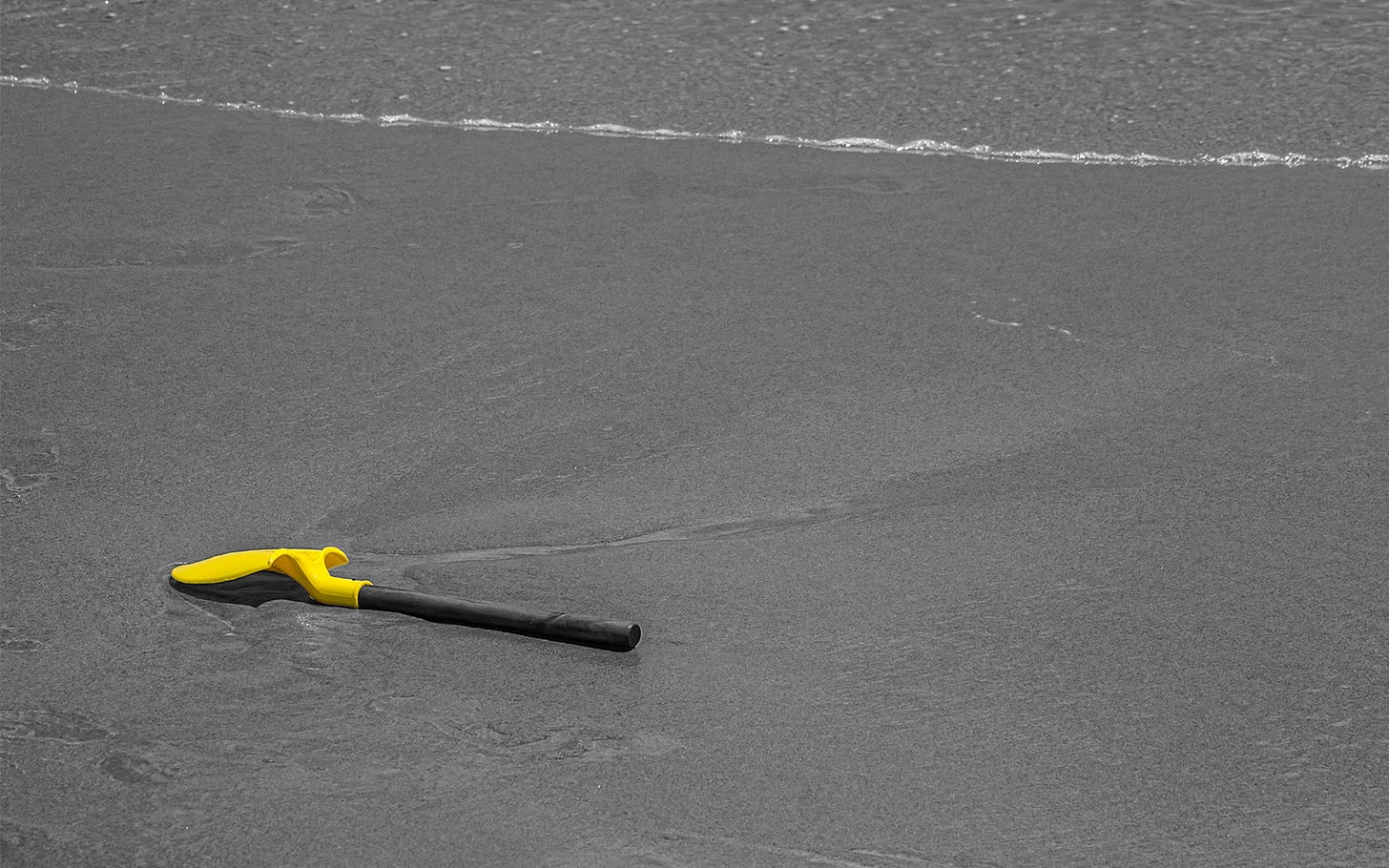 Lonely yellow shovel waits by the edge of the water