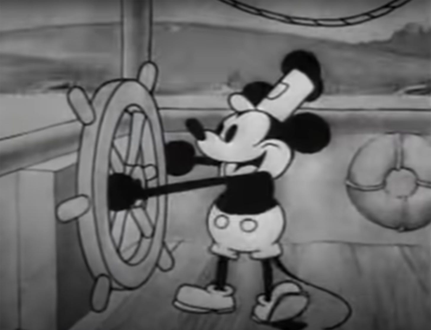 A still of Mickey Mouse from 'Steamboat Willie' showing him at the wheel of a ship.