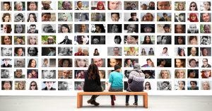 people sit on a bench in front of rectangles on wall of many faces
