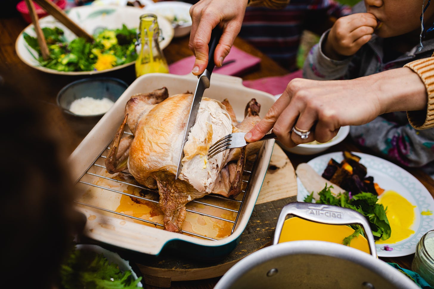 Hands cutting a roast chicken on a dinner table with children eating