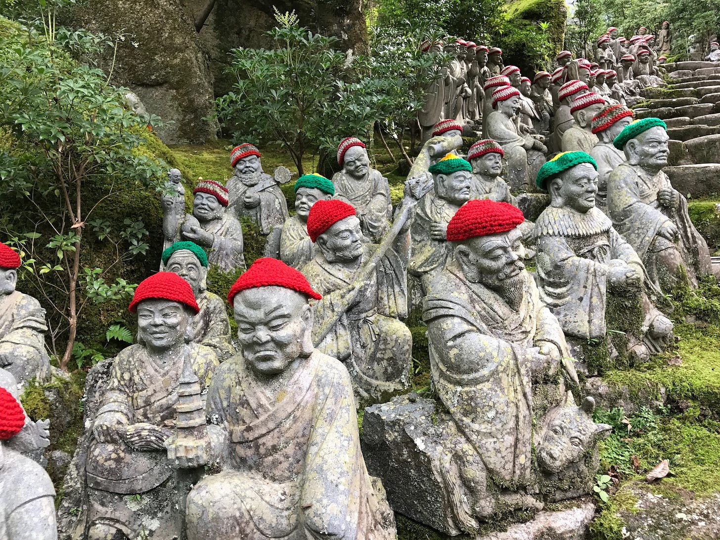 Fotografia em cores de estátuas religiosas de pedra em templo de Hiroshima. Algumas estátuas sorriem, outras têm expressão grave; algumas usam chapéus vermelhos, outras verdes. Fotografia em cores de estátuas religiosas de pedra em templo de Hiroshima. Algumas estátuas sorriem, outras têm expressão grave; algumas usam chapéus vermelhos, outras verdes.