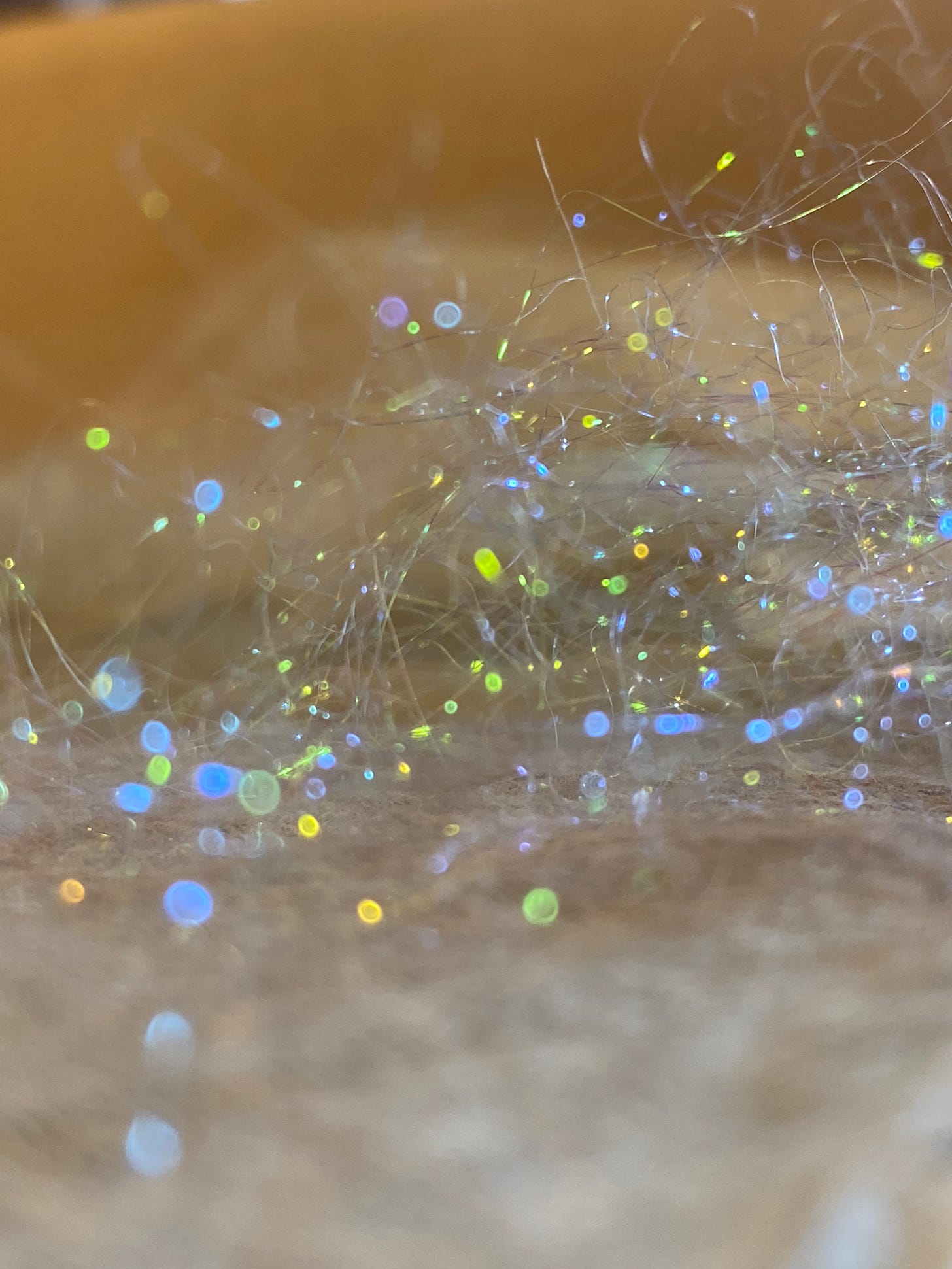 a closeup of fibre with coloured spots of light reflected in greens and blues, oranges and yellows