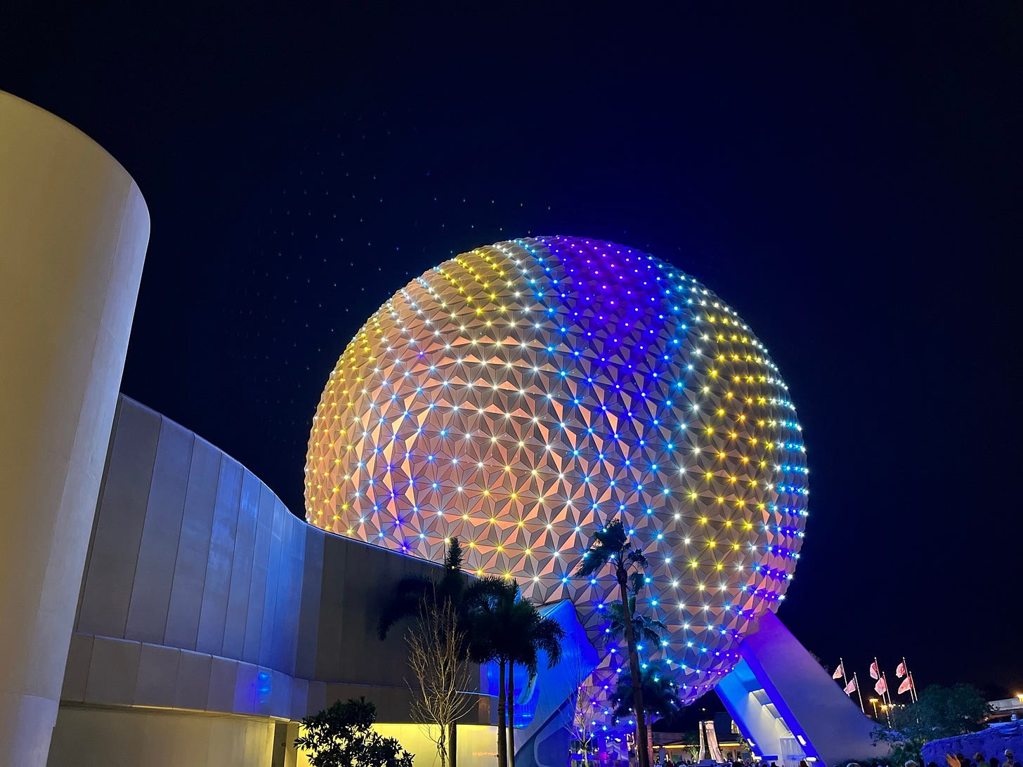 The iconic Epcot ball at night, lit up in many colors.