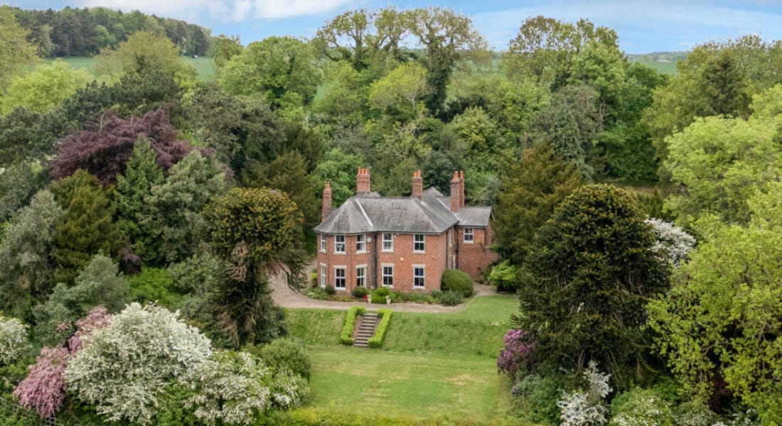 A large brick house with a lawn in front of it and trees around it