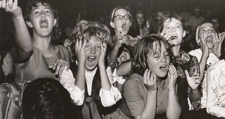 This may contain: a group of people sitting in the middle of a crowd with their hands up to their mouths