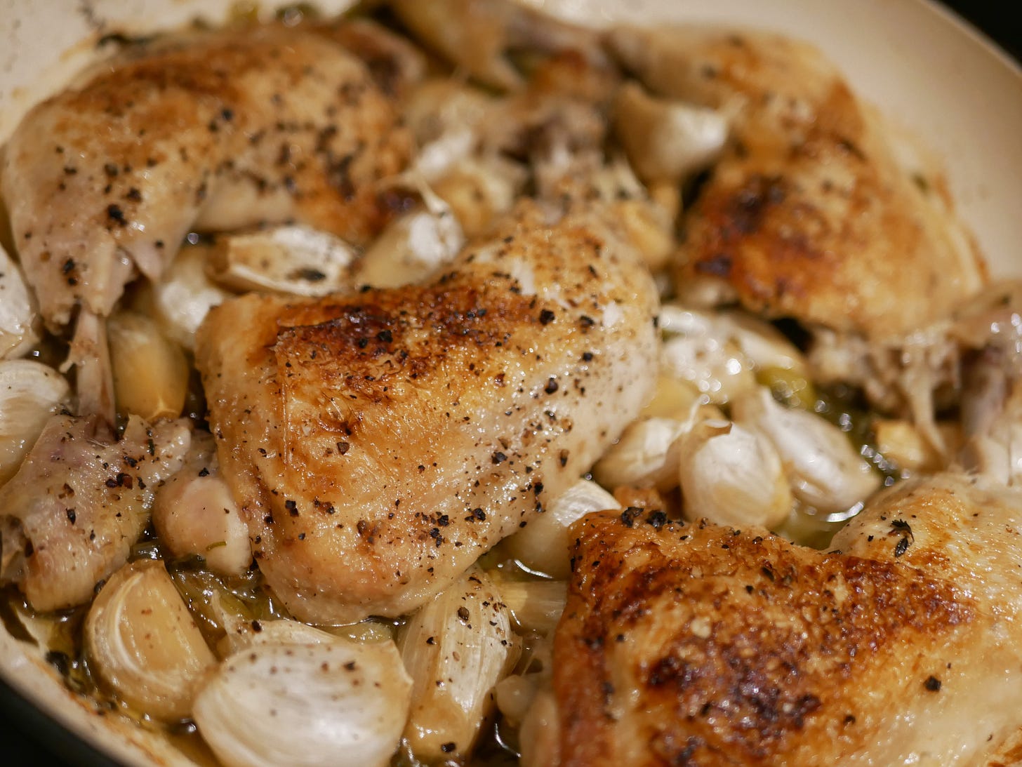 A close up of cooked chicken legs in a pan, alongside lots of roasted garlic.