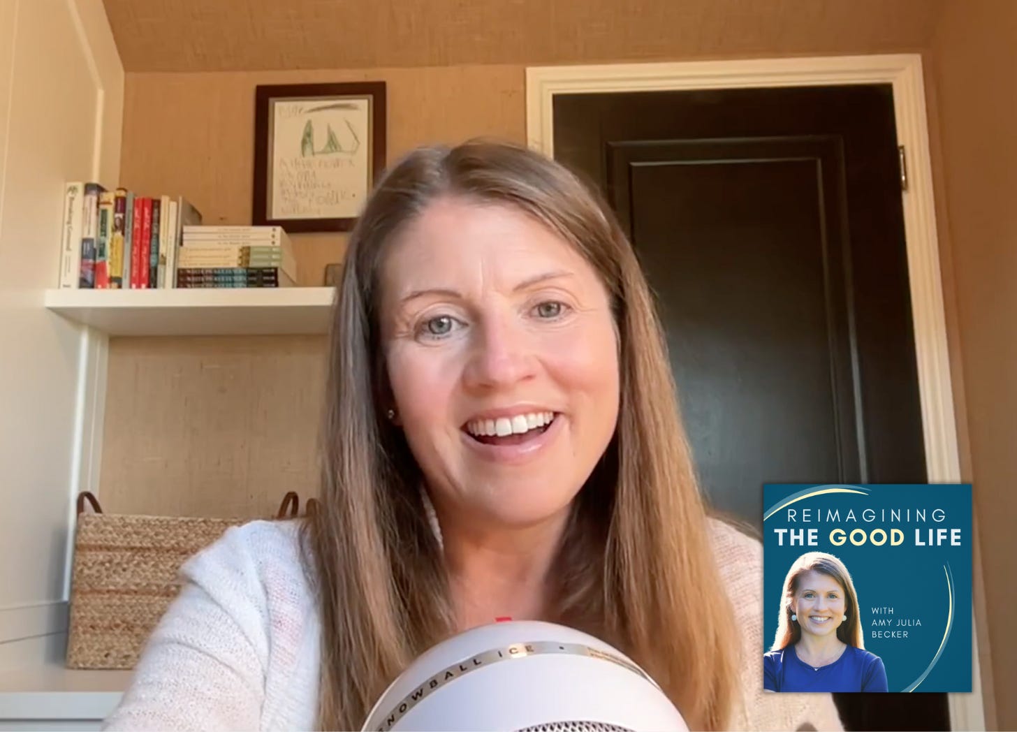 screenshot of Amy Julia recording a podcast. She is sitting in her office with a mic in front of her. She is smiling widely!