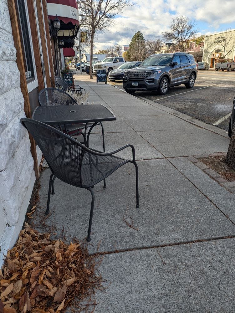 empty chairs and tables on a sidewalk in a little downtown