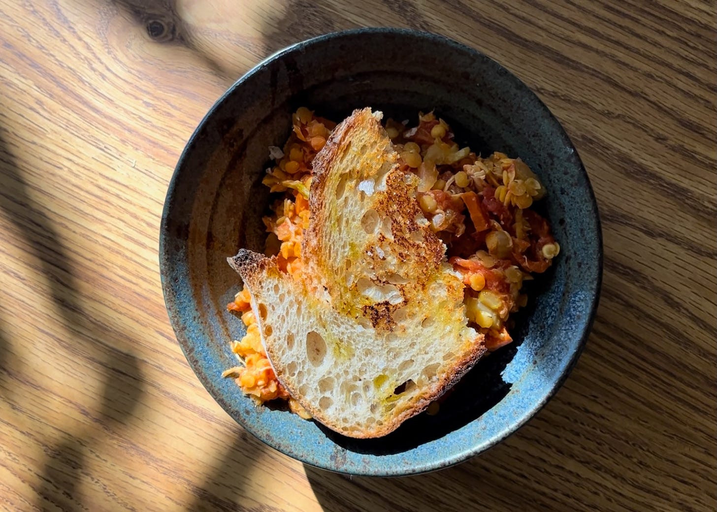 a blue bowl with lentil stew and a piece of toast on top