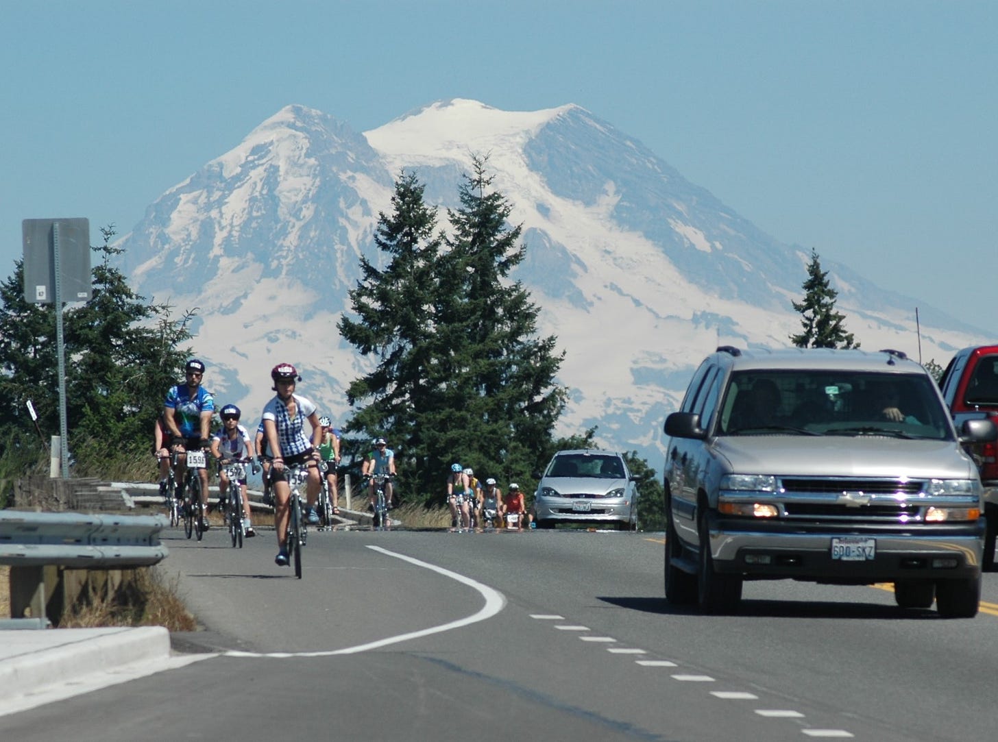 Bicycling on a highway edge with Mount Rainier behind.