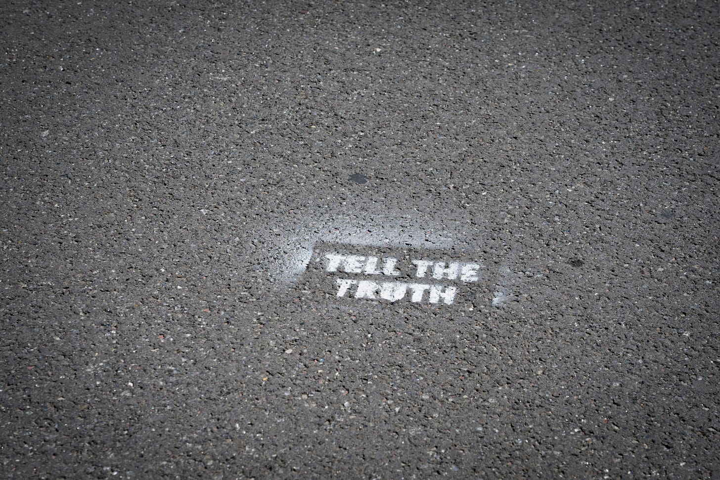 A grey concrete road with white stencilled graffiti that says 'tell the truth'