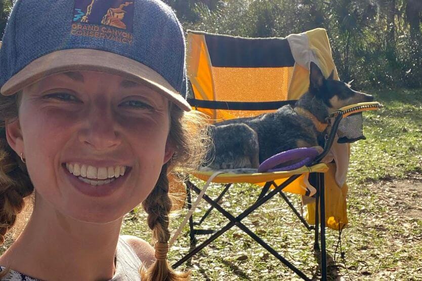 Haley sits on the ground in front of a yellow lawn chair that Scout the blue heeler lies on in the background