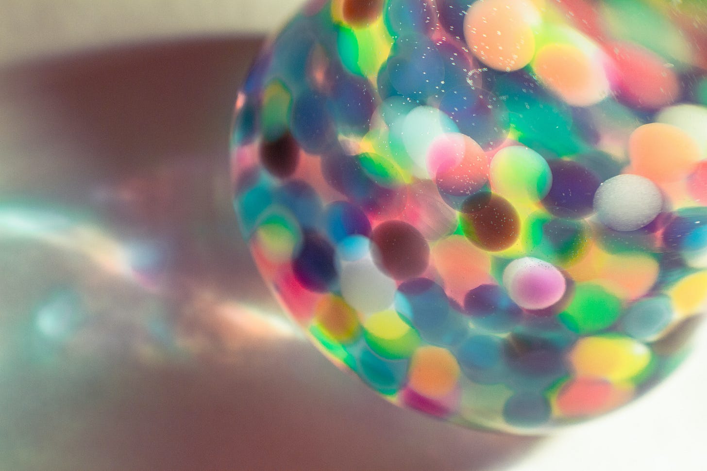 Photo of a sphere with overlapping rainbow colored circles casting a rainbow shadow on a pale background by Girl with Red Hat from Unsplash. 